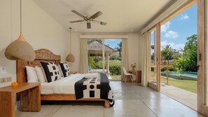 A bedroom with a bed, a ceiling fan, a wooden headboard, and a view of a swimming pool and garden. - Alea Estate by Villa Finder (Kerobokan)