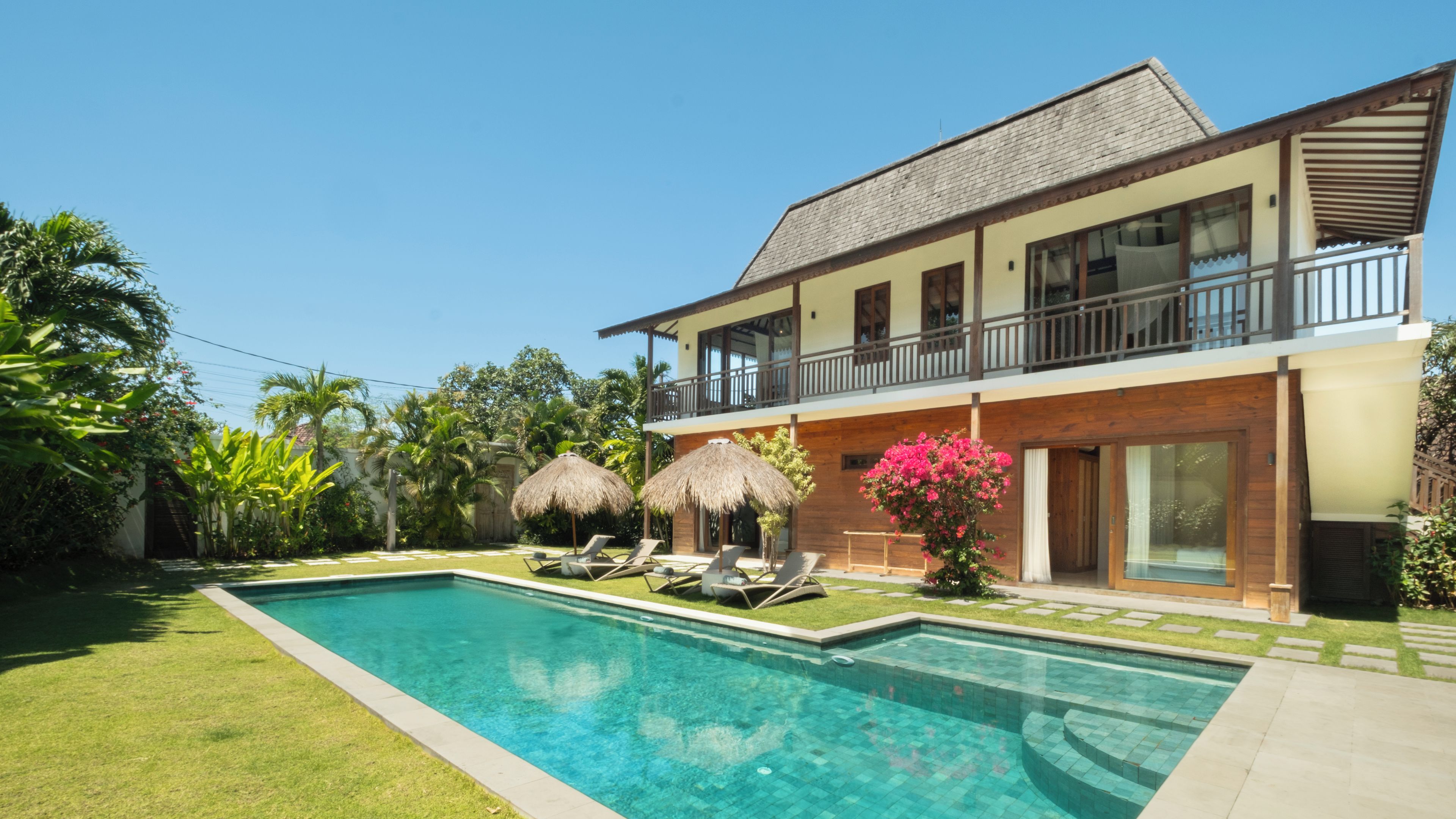 Una casa a due piani con piscina, un balcone e vegetazione tropicale.