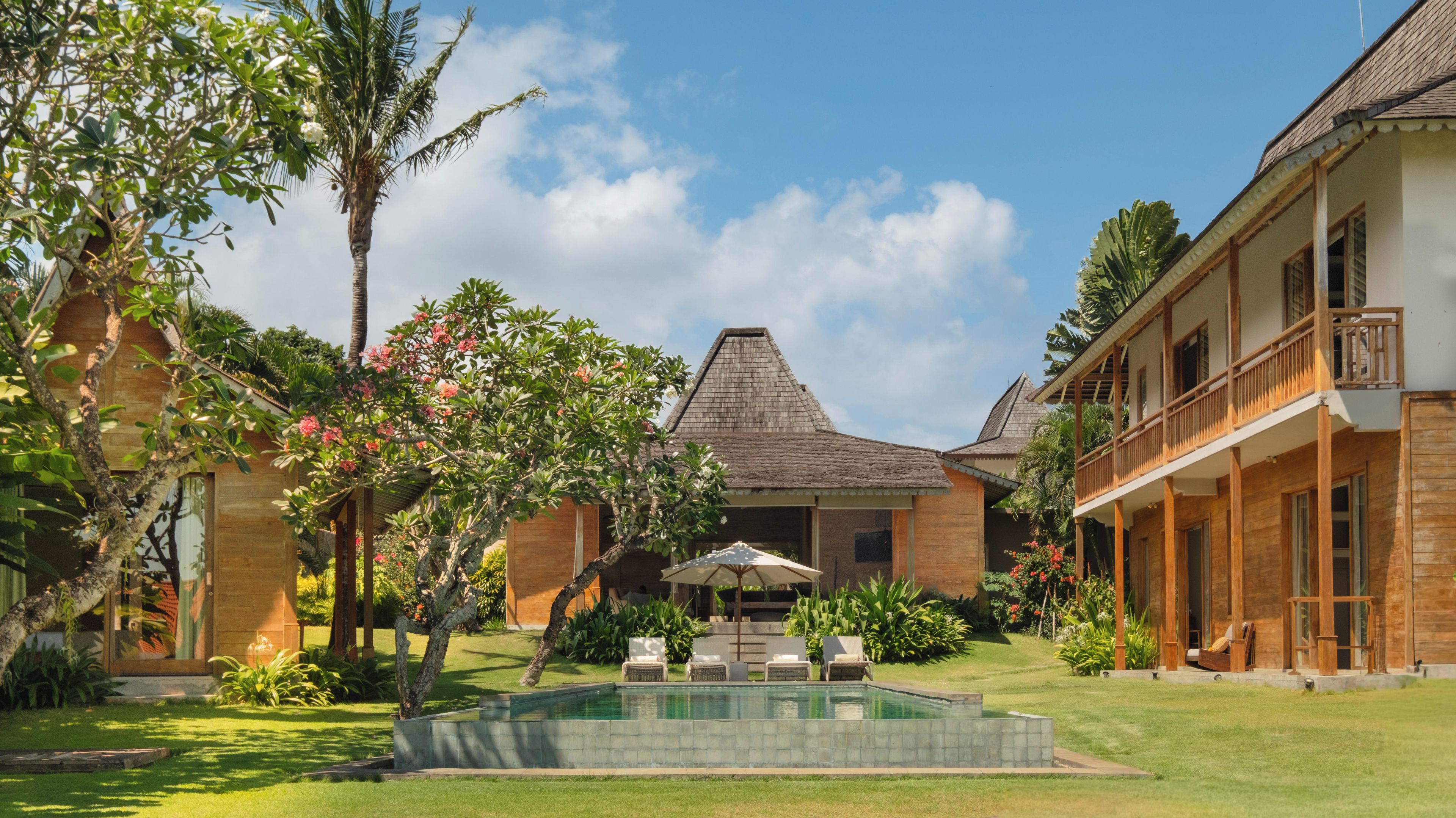 A residential property with a swimming pool, lush greenery, and a two-story building with a balcony.