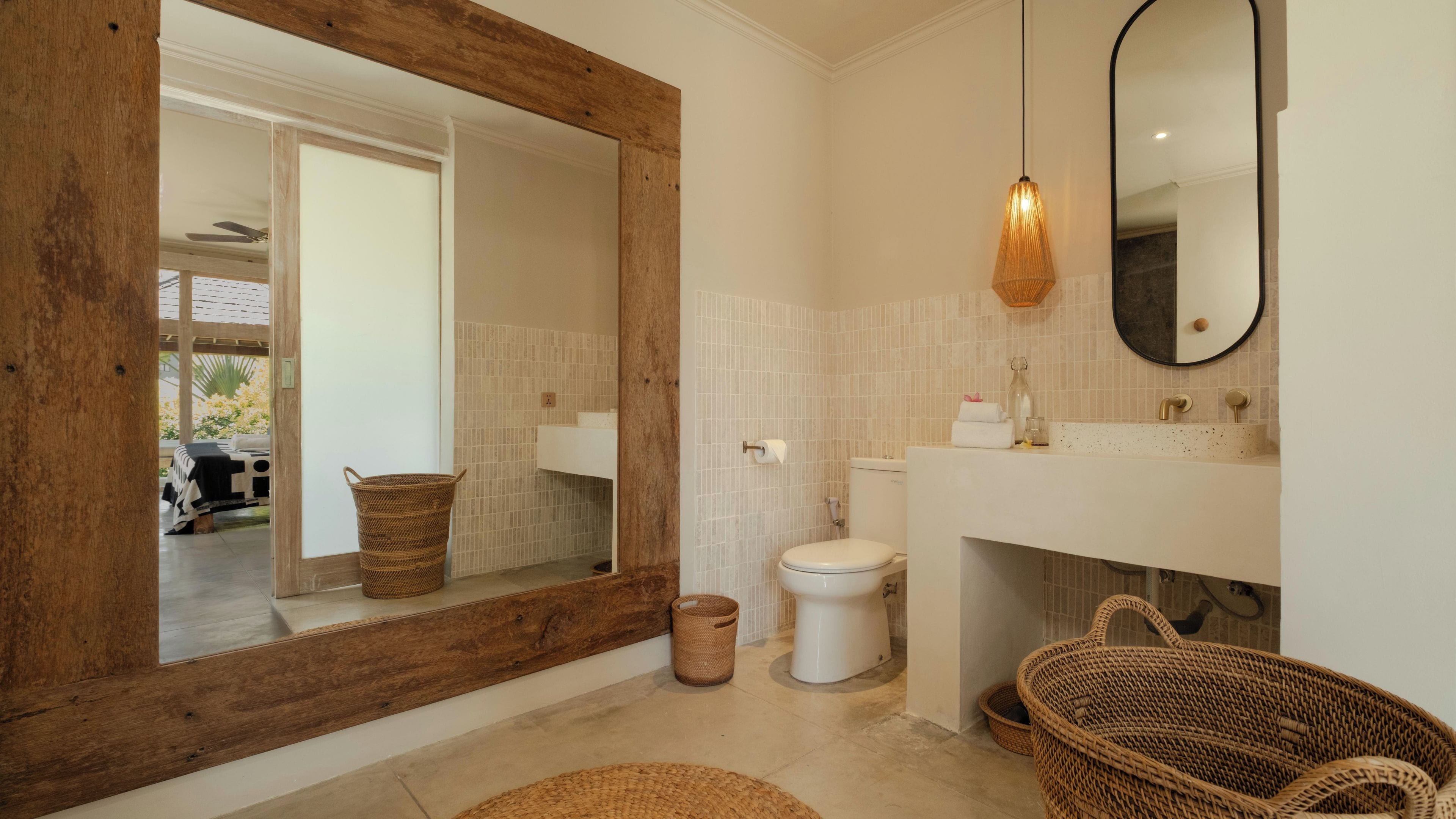 Ein Badezimmer mit einem spiegelnden Holzbettrahmen, weißen Fliesen, einem weißen Waschbecken und einer Pendelleuchte.