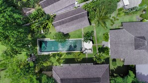 Vue aérienne d’un quartier résidentiel avec une piscine entourée d’une végétation luxuriante et de nombreuses maisons aux toits gris.