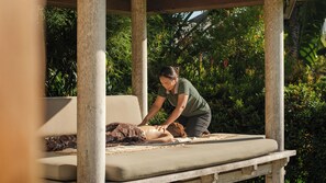 Een massagesessie op een houten bank met kussen, omgeven door weelderige begroeiing.