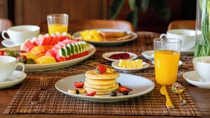 Een ontbijt met pannenkoeken, fruit en sinaasappelsap op een tafel.