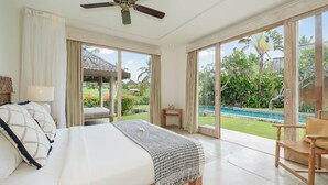 A spacious bedroom with a large bed, a ceiling fan, and a view of a swimming pool and garden. - Alea Estate by Villa Finder (Kerobokan)
