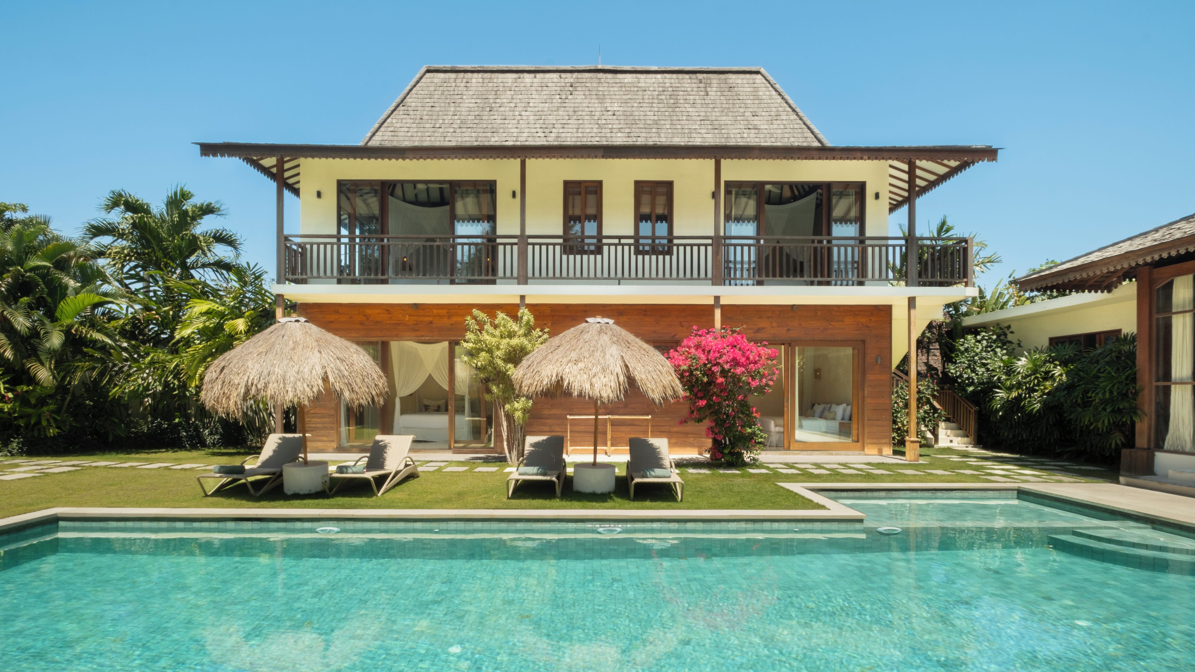 A two-story building with a swimming pool, lounge chairs, and thatched umbrellas.