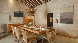 A dining area with a long wooden table, wicker chairs, and a hanging light fixture. - Alea Estate by Villa Finder (Kerobokan)