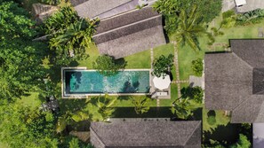 Vue aérienne d’un quartier résidentiel avec une piscine rectangulaire entourée d’une végétation luxuriante et de quelques bâtiments aux toits gris.