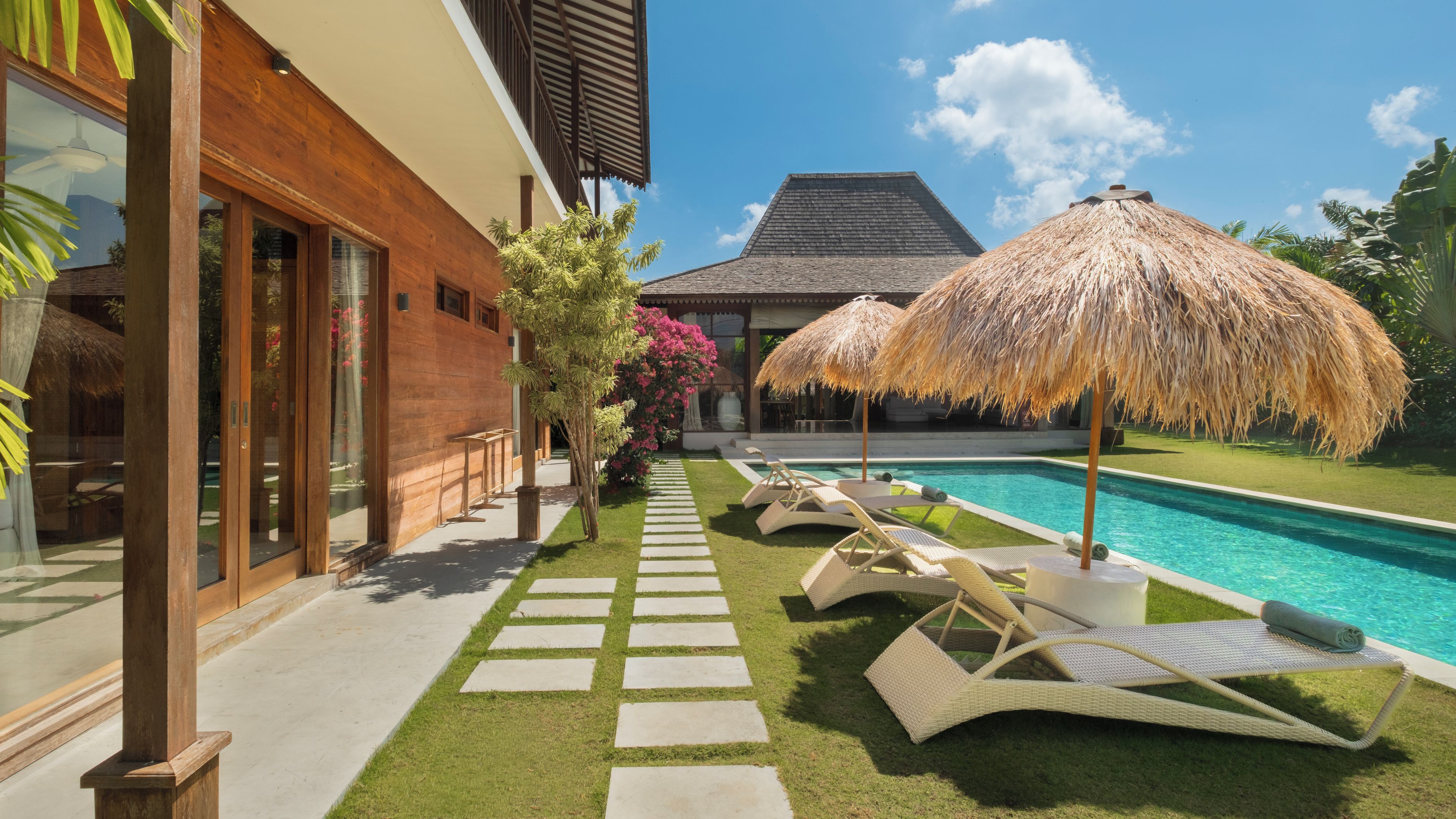 A poolside area with lounge chairs, a thatched umbrella, and a wooden building with large windows.