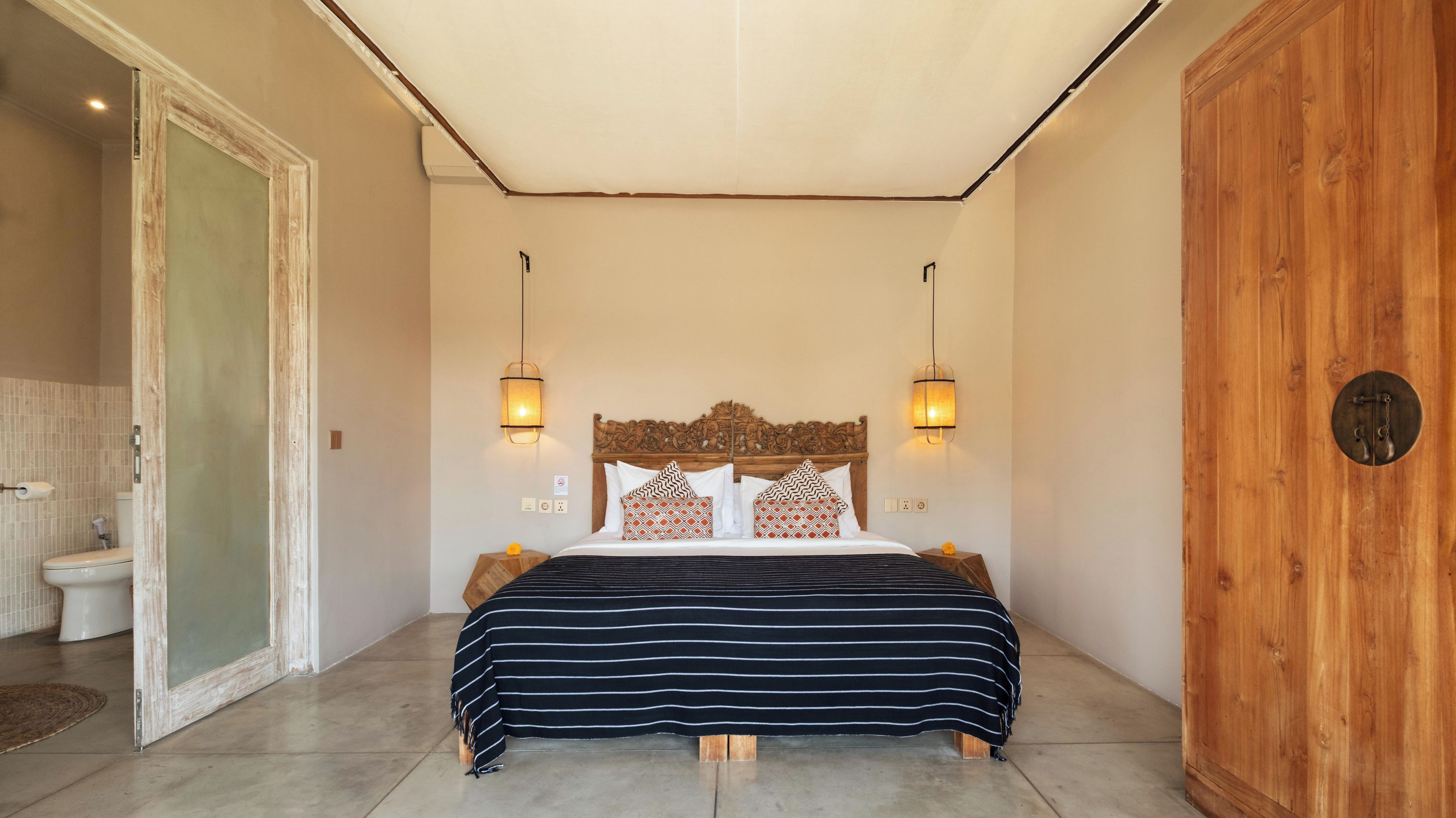 Ein Schlafzimmer mit Holz-Kopfteil, zwei Nachttischlampen, einem Bett mit gestreifter Bettwäsche und einem Holzschrank.