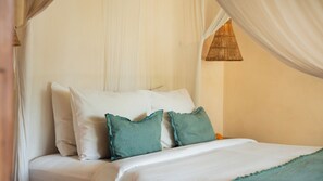 A bed with white linens and two teal pillows, a woven rattan lamp, and sheer curtains.