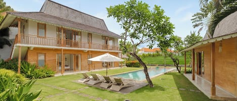A two-story house with a swimming pool, a covered patio, and a well-maintained lawn.