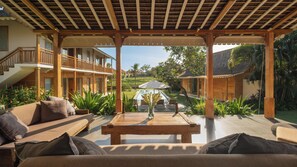 A covered outdoor seating area with a pool, wooden furniture, and a view of a residential building.