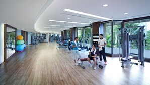 A spacious gym with various exercise equipment, large windows, and a wooden floor.