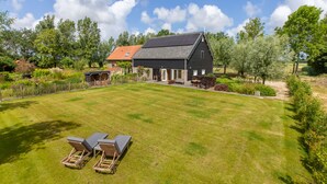 A house with a large lawn, two lounge chairs, and a garden with various plants.