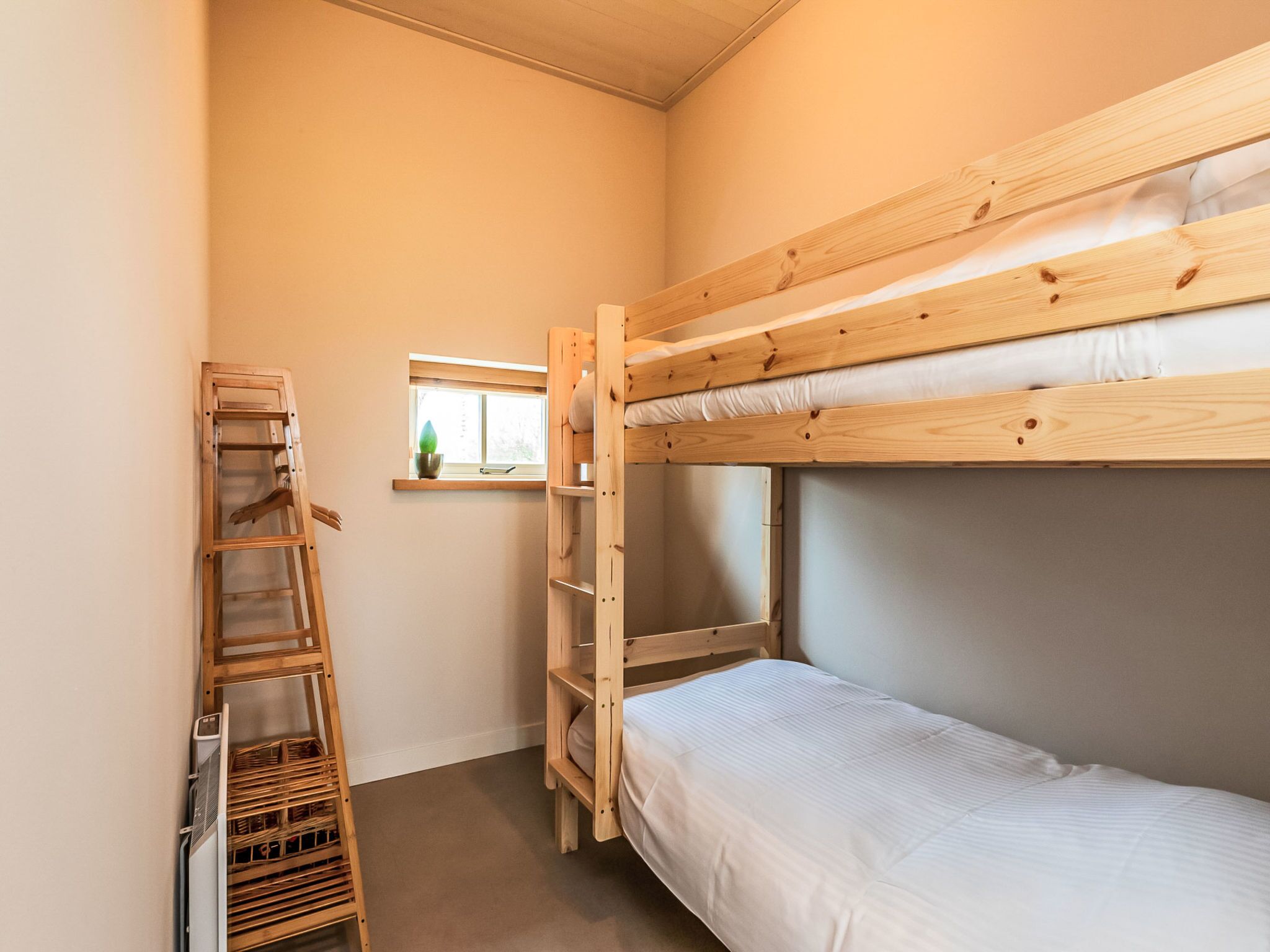 Een slaapkamer met een stapelbed, een raam, een houten ladder en een plankunit.