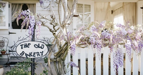 A rustic wooden building with a sign reading 'THE OLD BAKERY' and a white picket fence.