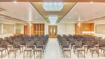 A conference room with rows of chairs, a large screen, and a chandelier.