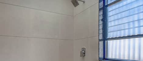 A modern bathroom with a toilet, a shower, and a window with blinds.