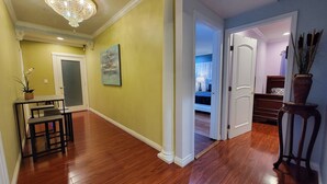 A hallway with wooden flooring, a chandelier, a painting, and a door leading to a bedroom.
