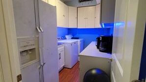 A compact kitchen with white cabinets, a refrigerator, a washing machine, and a microwave.