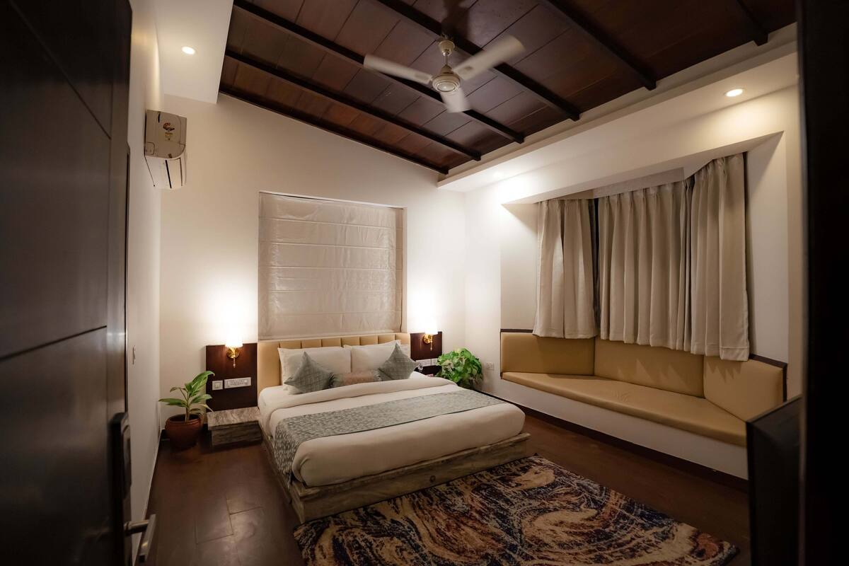 Une chambre à coucher comprenant un lit, un canapé, un ventilateur de plafond, une fenêtre avec des rideaux et un climatiseur fixé au mur.
