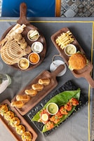 Variedad de alimentos en tablas de madera, incluyendo pan plano, papas fritas, hamburguesas y samosas.