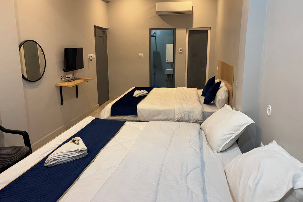 A hotel room with two beds, a TV, a mirror, and a small table.