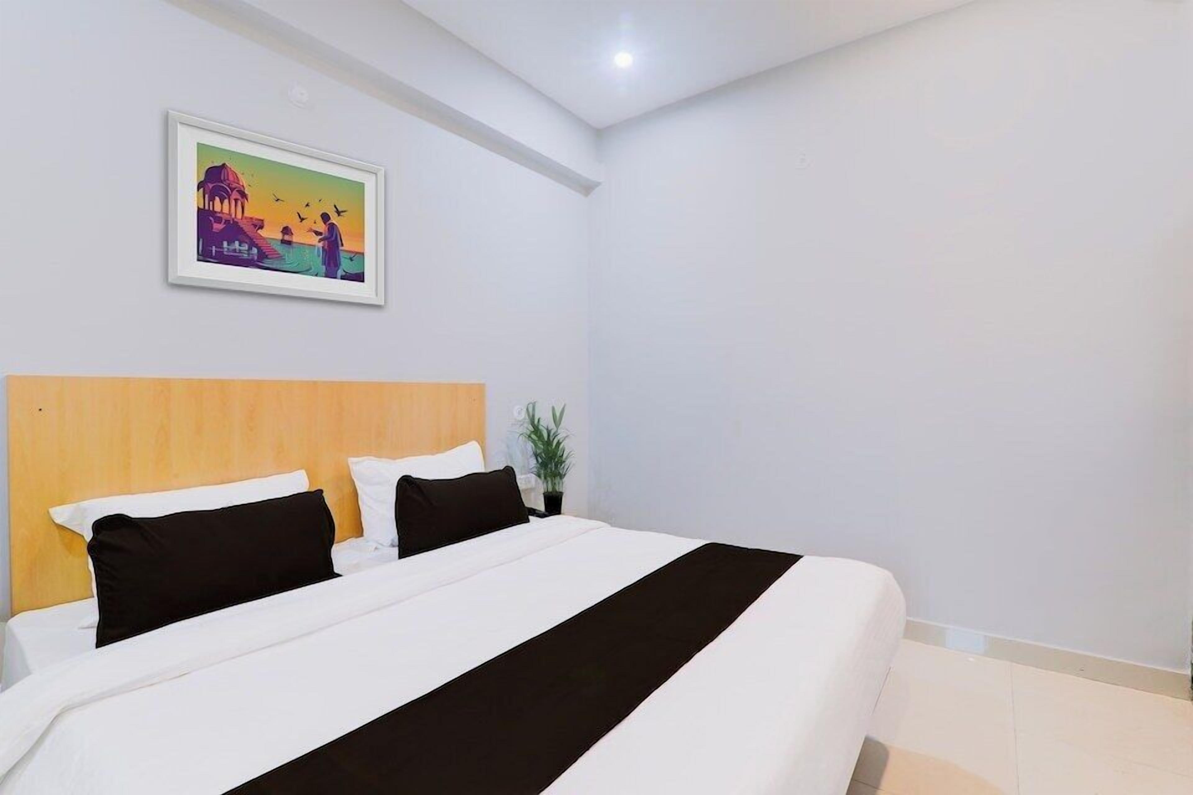 Une chambre d’hôtel avec un grand lit, une tête de lit en bois, un tableau encadré au mur et une petite plante en pot.