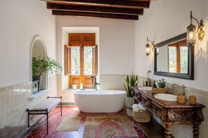 A bathroom with a freestanding bathtub, a vanity with a mirror, and a large window. - Hotel Boutique Los Remedios (Comonfort)