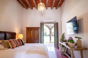A bedroom with a bed, a wooden wardrobe, a desk with a vase, and a TV on the wall. - Hotel Boutique Los Remedios (Comonfort)