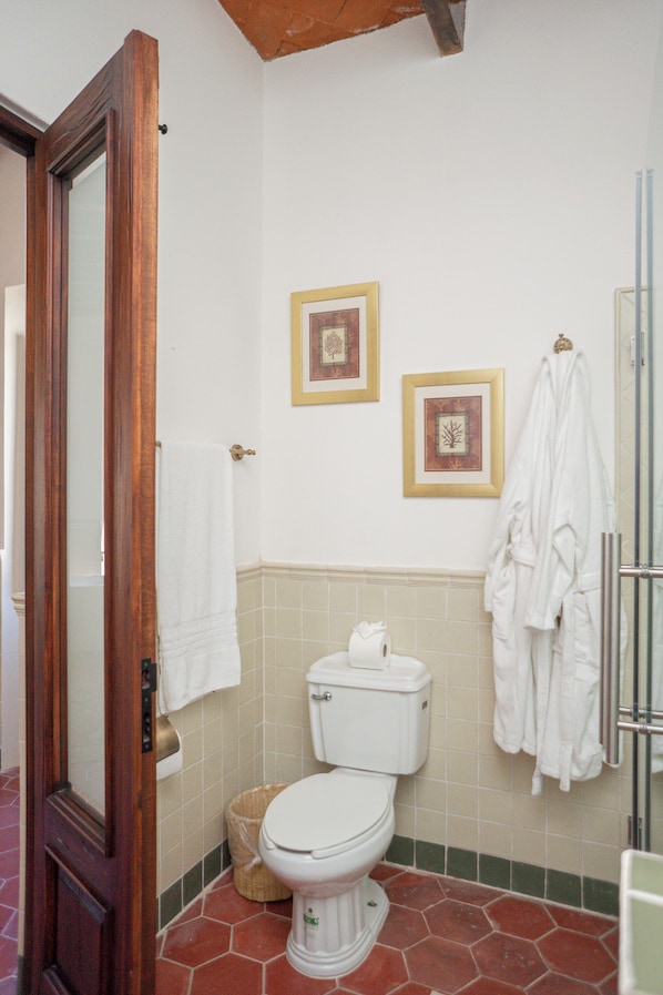 A bathroom with a toilet, a wooden door, a white towel, and a framed picture on the wall.
