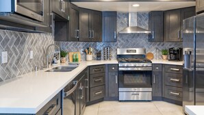 Een moderne keuken met donkere kastjes, roestvrijstalen apparatuur en een backsplash van visgraatmozaïek.