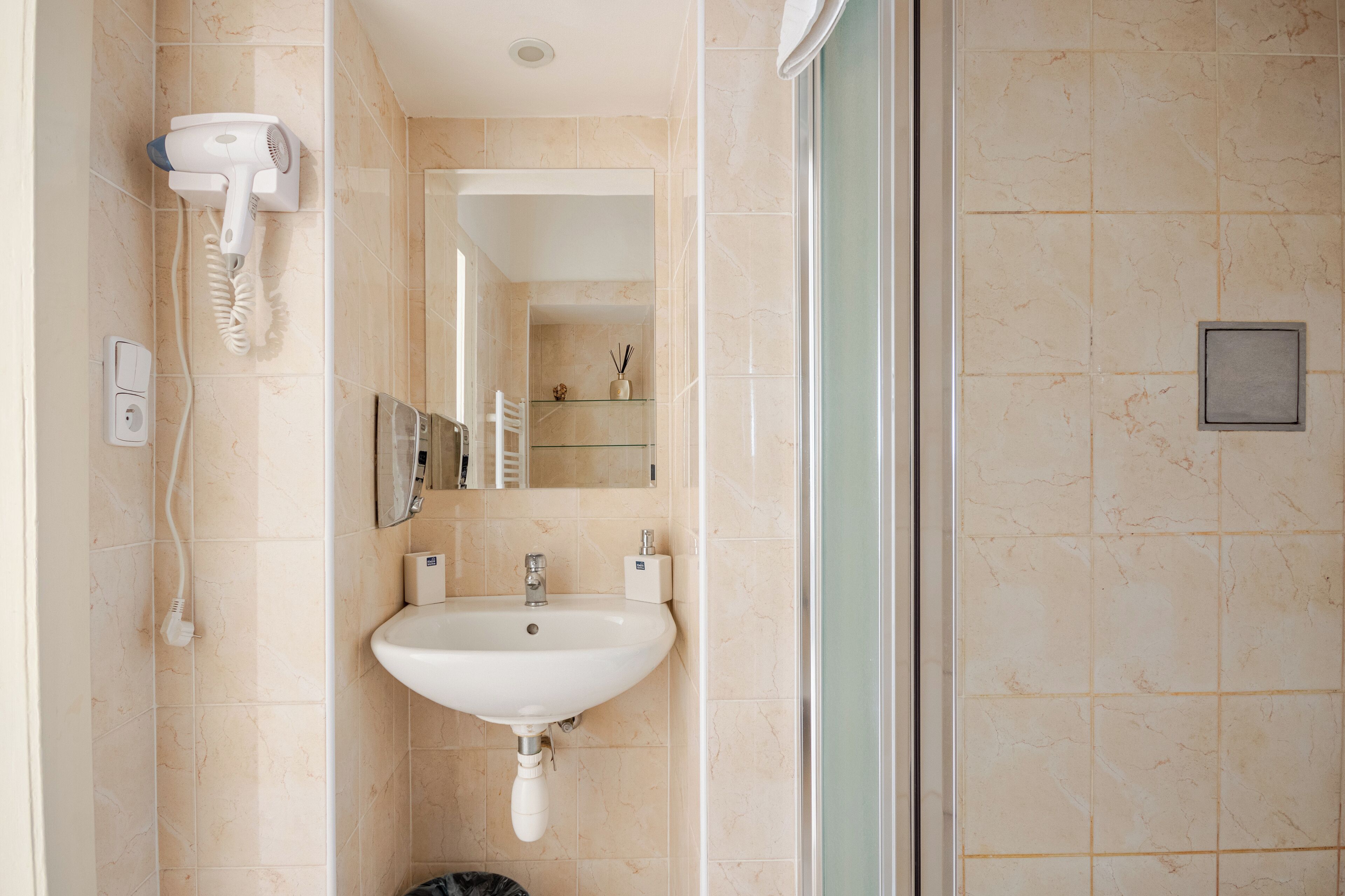 A bathroom with a white sink, a hairdryer mounted on the wall, and a mirror above the sink.