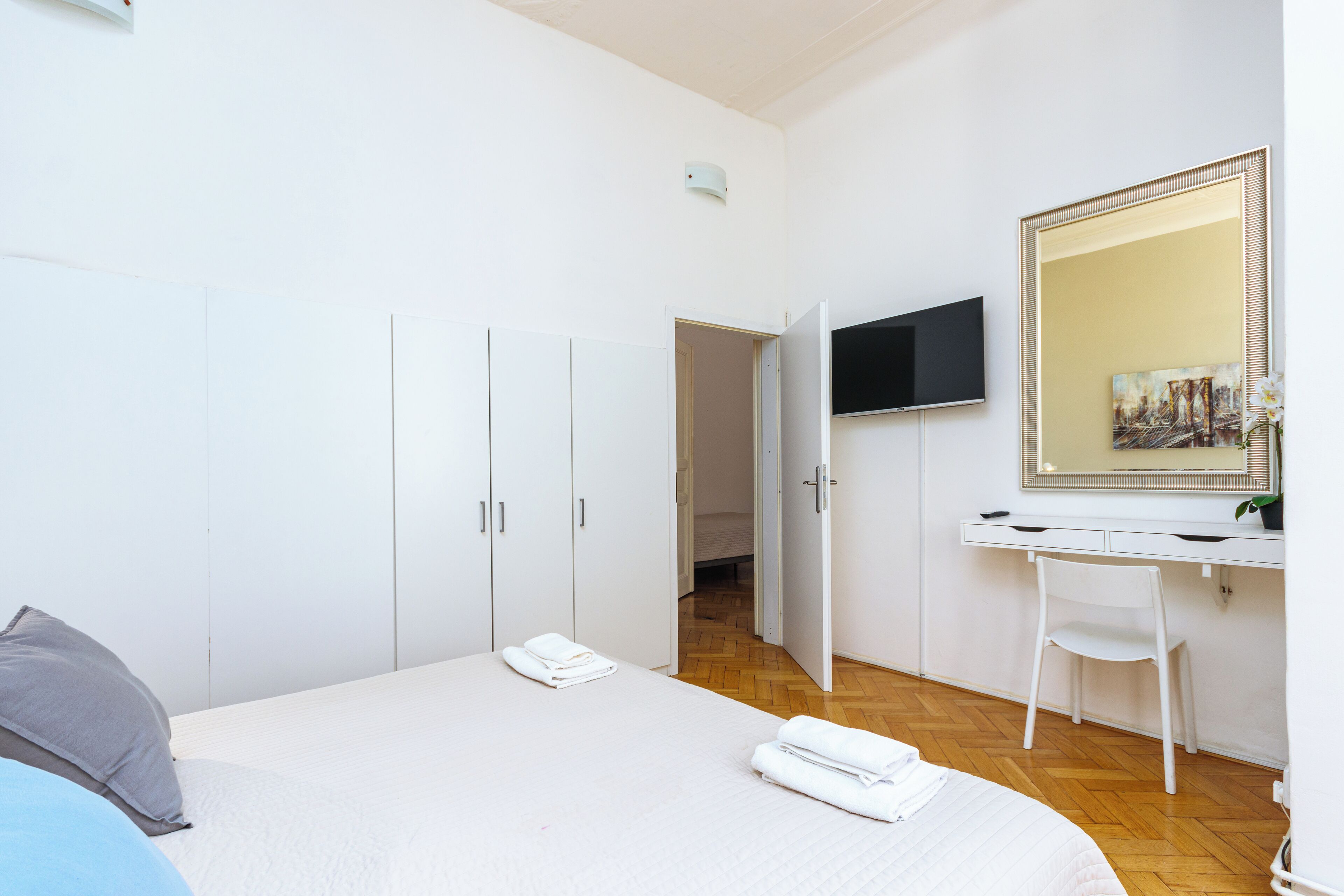 A bedroom with a bed, a desk, a chair, a TV, and a large mirror.