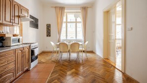 A kitchen with wooden cabinets, a microwave, and a stove. There is a dining table with chairs and a window with curtains. - Vincanto Apartments Oldtown Prague 1 (Prague)