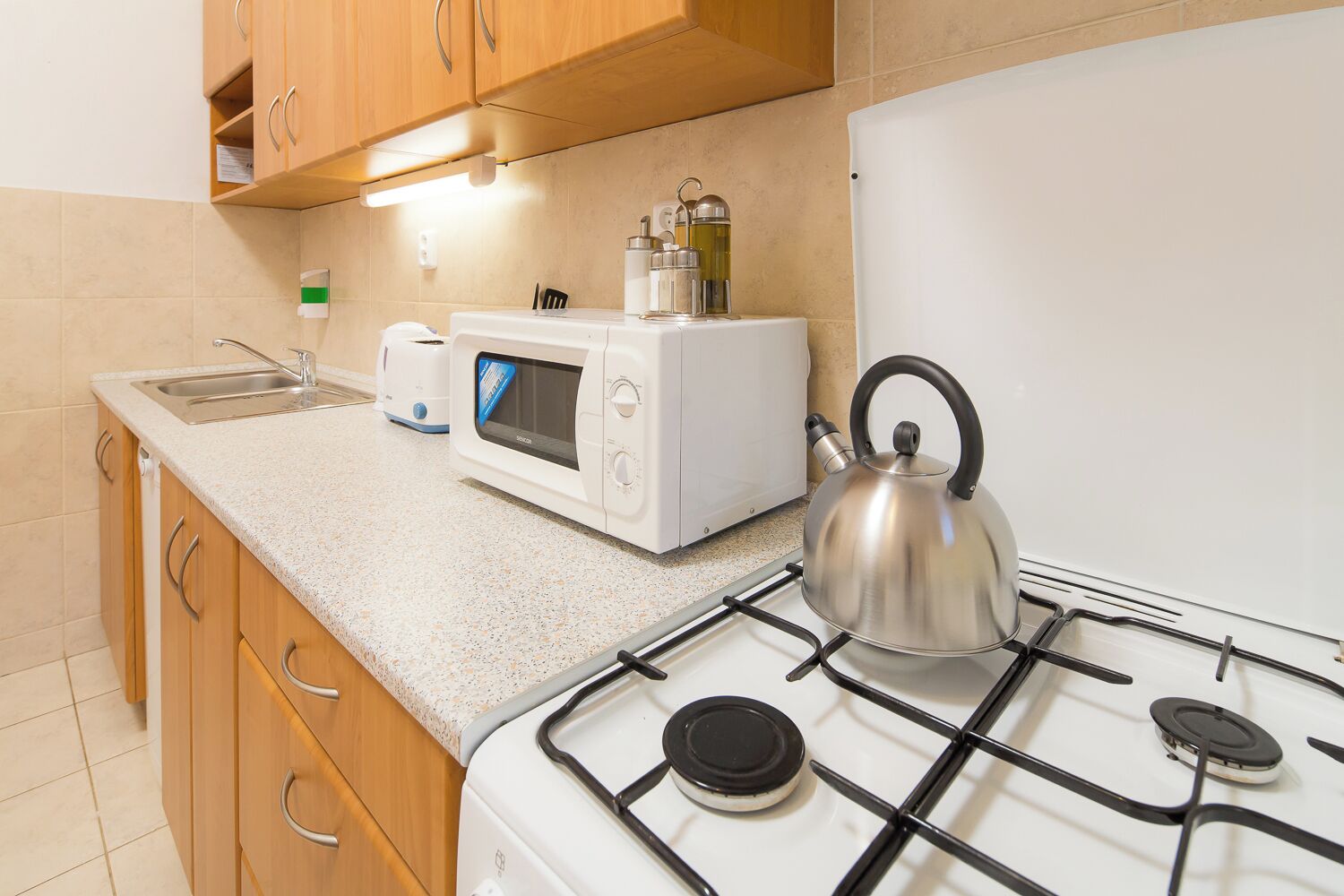 Une cuisine compacte équipée d’une cuisinière à gaz, d’une bouilloire, d’un four à micro-ondes et d’un grille-pain.