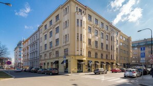 A multi-story building with a classic architectural style, featuring a ground-floor commercial area with shops and a parking sign indicating a nearby parking facility. - Vincanto Apartments Oldtown Prague 1 (Prague)