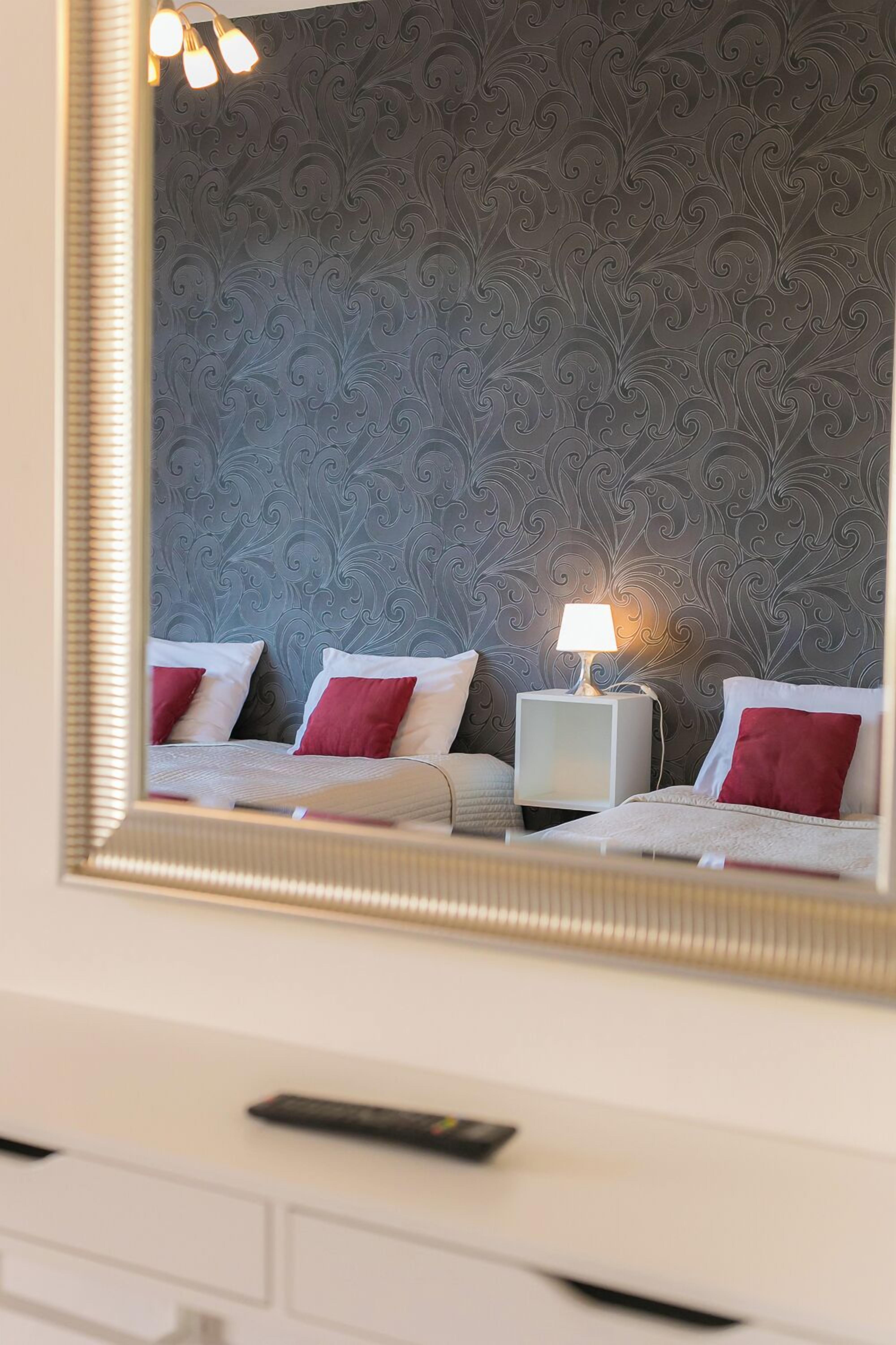 A hotel room with a bed, a nightstand with a lamp, and a mirror reflecting the room.
