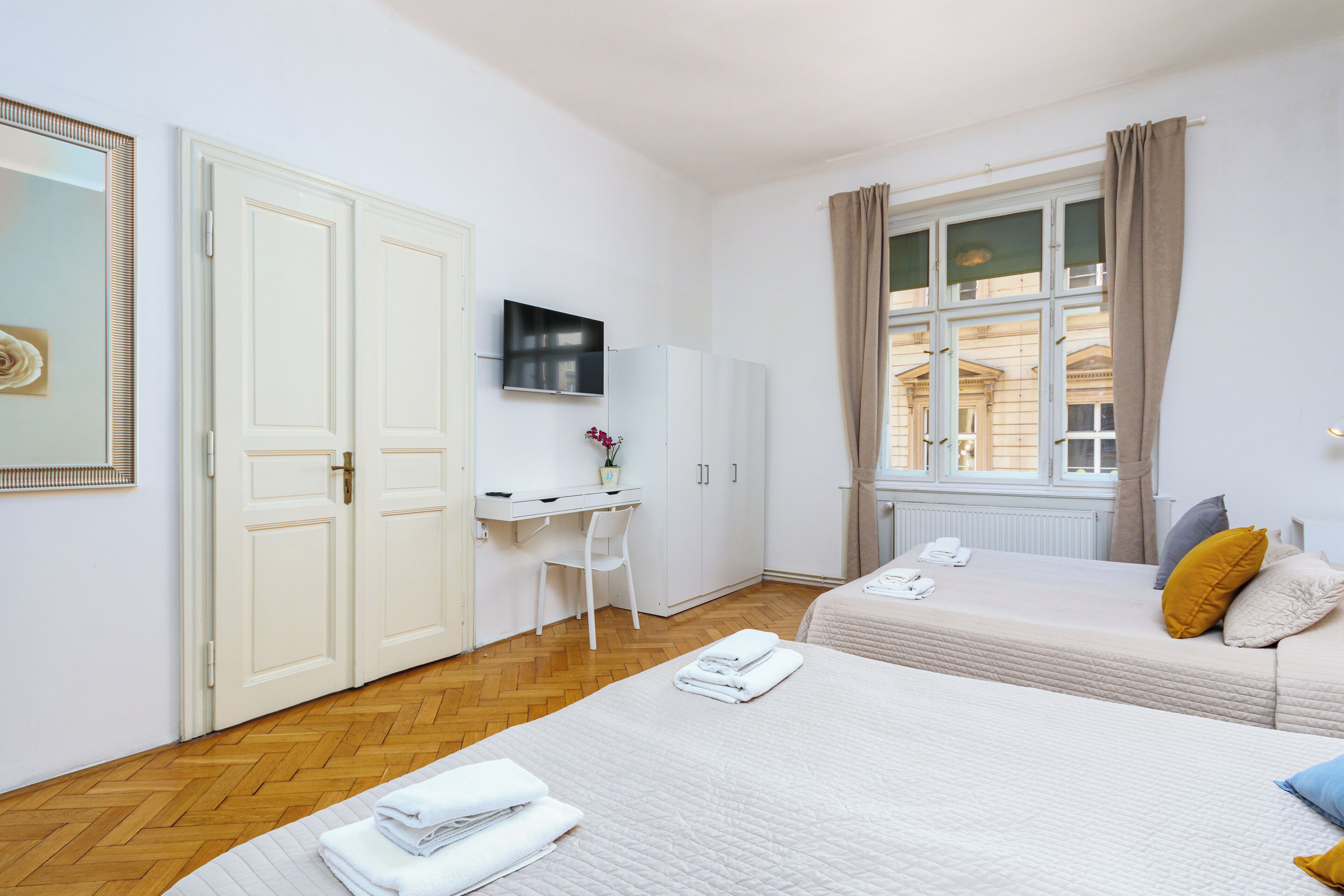 A hotel room with two beds, a desk, a TV, and a window with curtains.