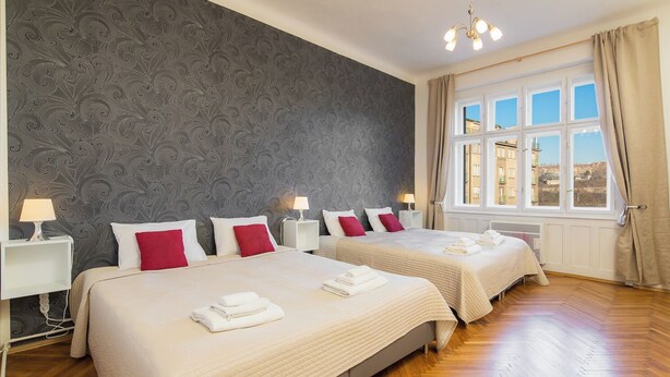 A hotel room with two beds, a patterned wallpaper, a large window with a view, and a chandelier. - Vincanto Apartments Oldtown Prague 1 (Prague)
