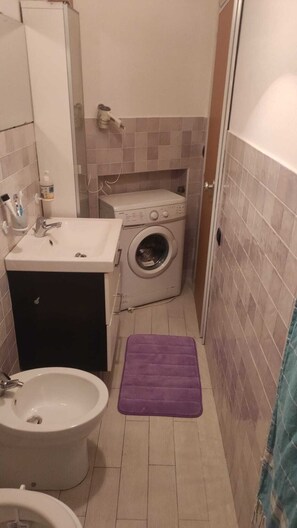 Compact bathroom with sink, toilet, bidet, and washing machine, featuring a comfortable floor mat.