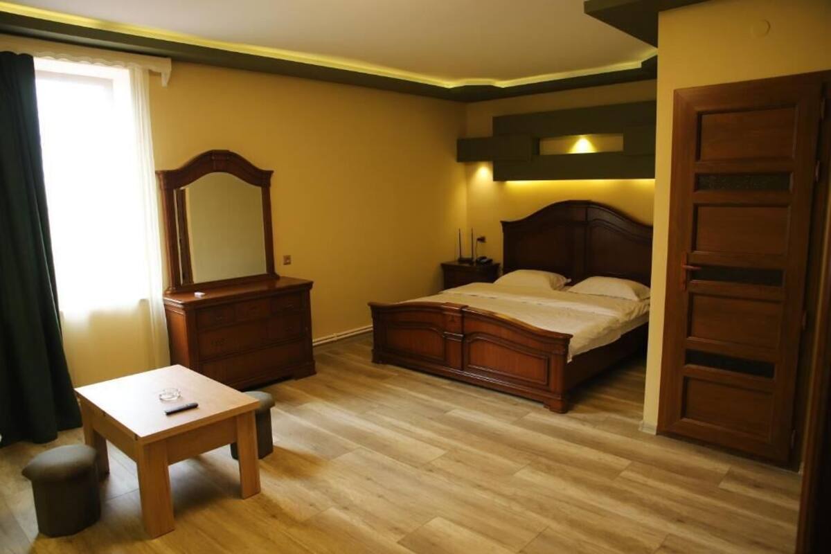 A bedroom with a wooden bed, a nightstand, a dresser, a mirror, and a small table.