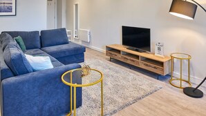 A modern living room with a blue sofa, a TV, a wooden entertainment unit, and a lamp. - Host Stay Mariposa Waterloo (Liverpool)