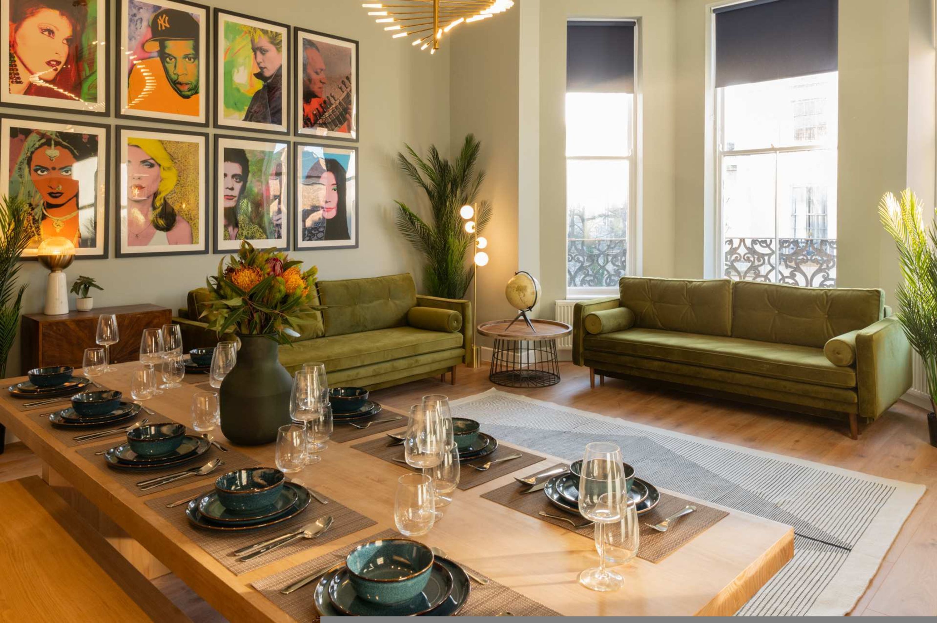 A dining area with a long table set for six, green sofas, and framed artwork on the walls.