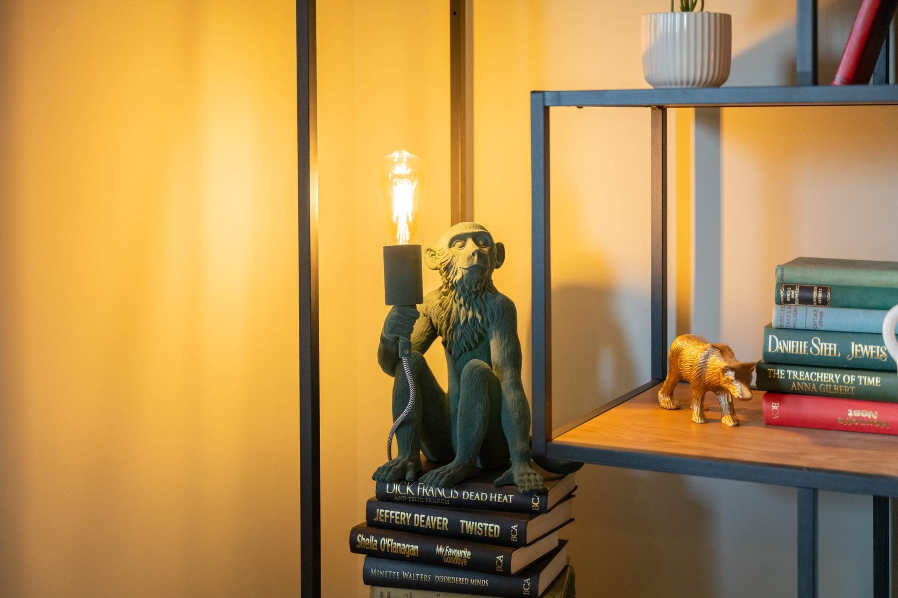 Ein Bücherregal mit einer Statue eines Mannes, der ein Telefon, eine Glühbirne und einen Stapel Bücher hält.