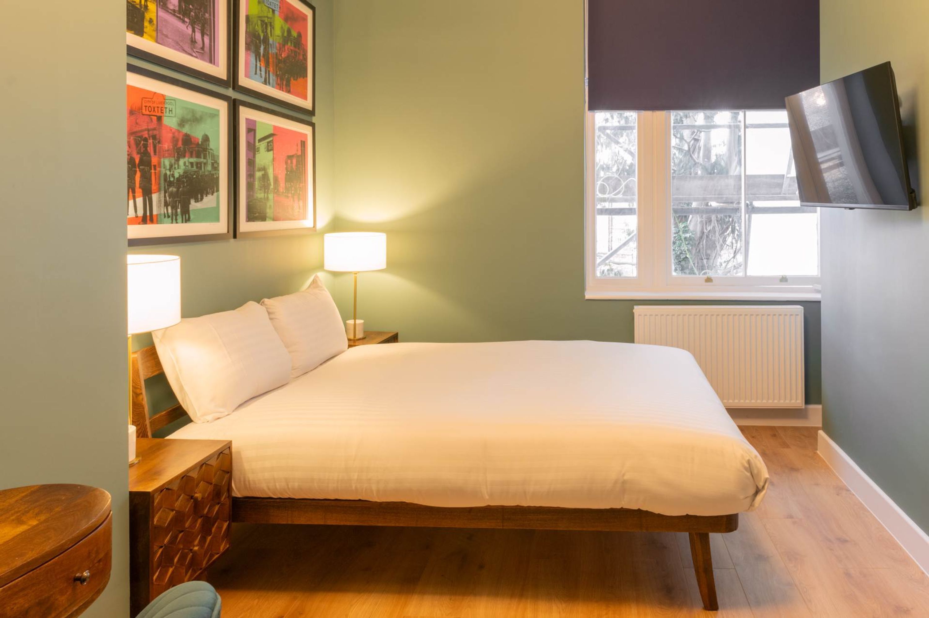 Une chambre à coucher avec un lit, des lampes de chevet, un téléviseur fixé au mur et des tableaux encadrés accrochés au mur.