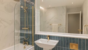 Ein modernes Badezimmer mit einer gläsernen Dusche, einem weißen Waschbecken und Wänden mit Marmoroptik.