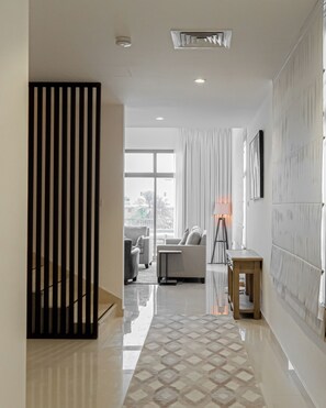 Enter a stylish hallway leading to a comfortable living area with a sofa set, floor lamp, and patterned rug.