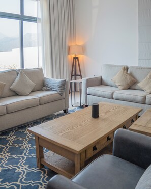 Relax in this inviting living room with two sofas, a coffee table, and a floor lamp, surrounded by sheer curtains and a patterned rug.