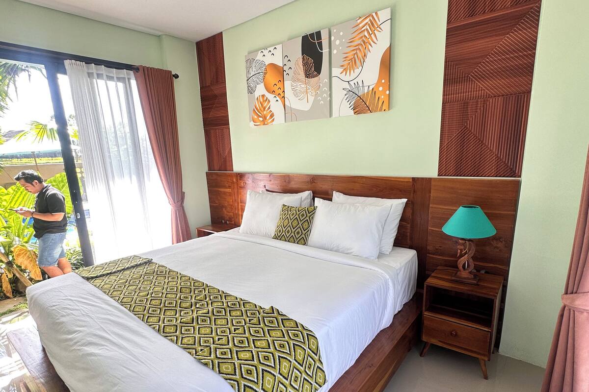 A spacious bedroom with a large bed, wooden headboard, and a nightstand with a lamp.